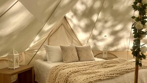 Un alloggio in tenda con un letto, cuscini, una coperta e due lanterne.