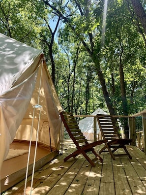A tented accommodation with a wooden deck, a chair, and a view of the forest.