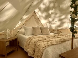 A tented accommodation with a bed, pillows, a blanket, and two lanterns.