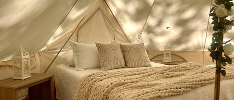 A tented accommodation with a bed, pillows, a blanket, and two lanterns.