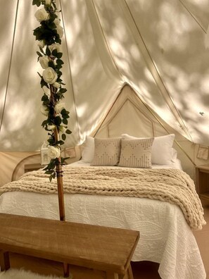 A tented accommodation with a bed, pillows, and a decorative plant.