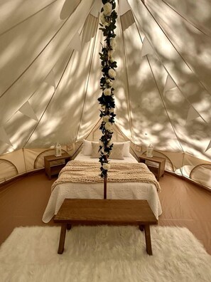 A tented accommodation with a bed, wooden nightstands, and a white fluffy rug.