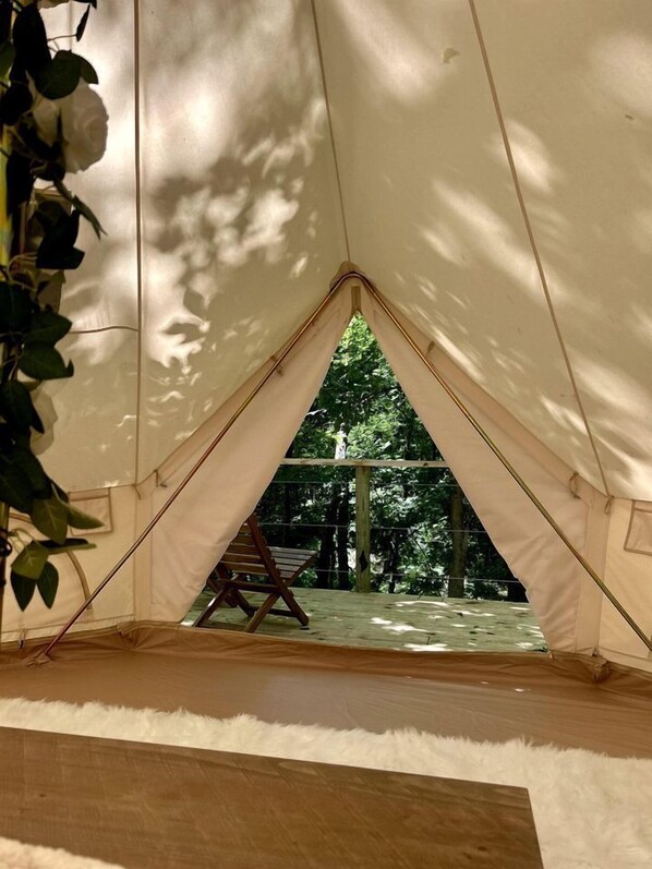 Una carpa con entrada triangular, suelo de madera y una silla en el exterior.