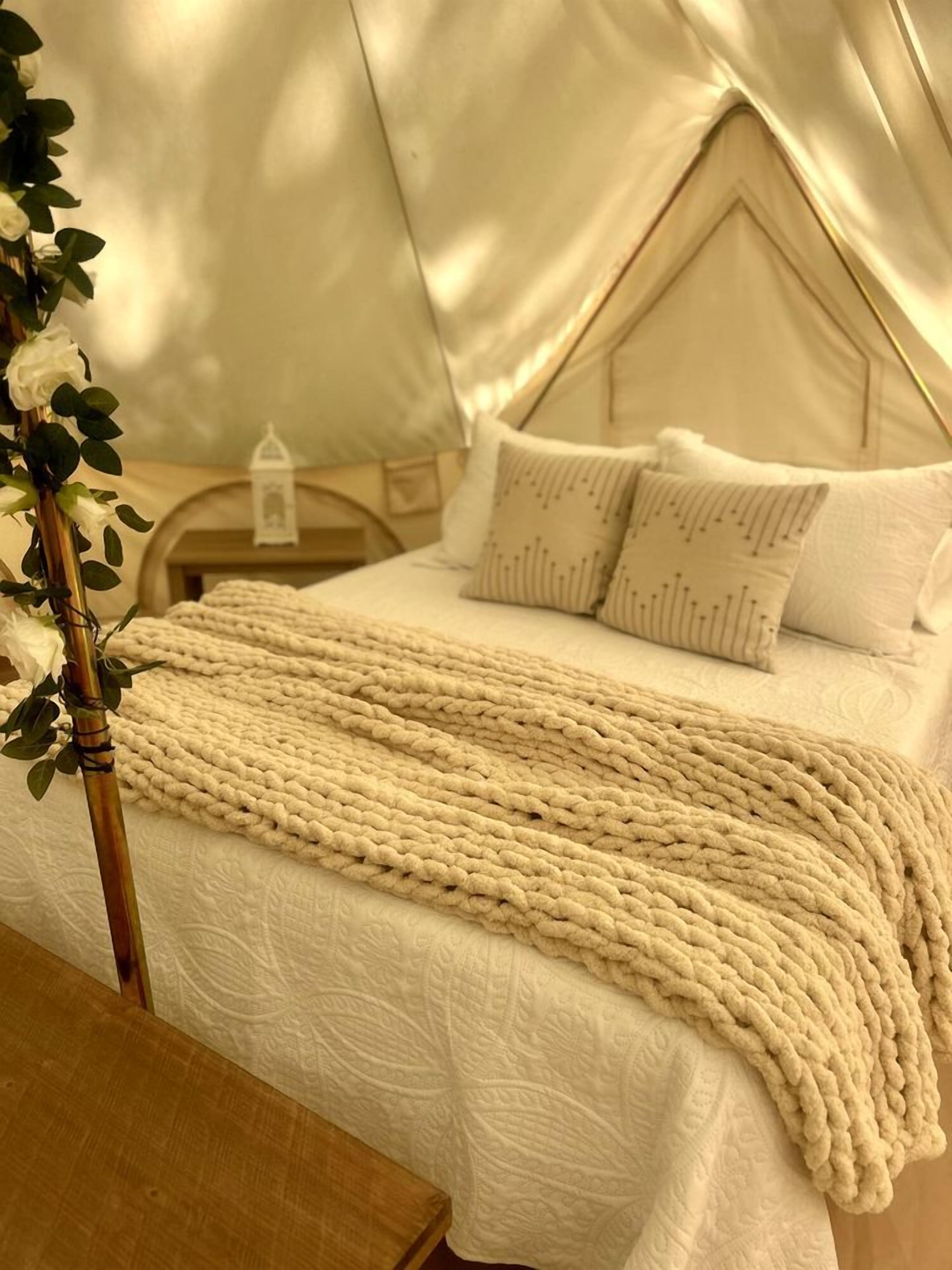 A tented room with a bed, pillows, a blanket, and a bedside table.