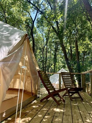 Alojamiento en una tienda de campaña con terraza de madera, una silla y vistas al bosque.