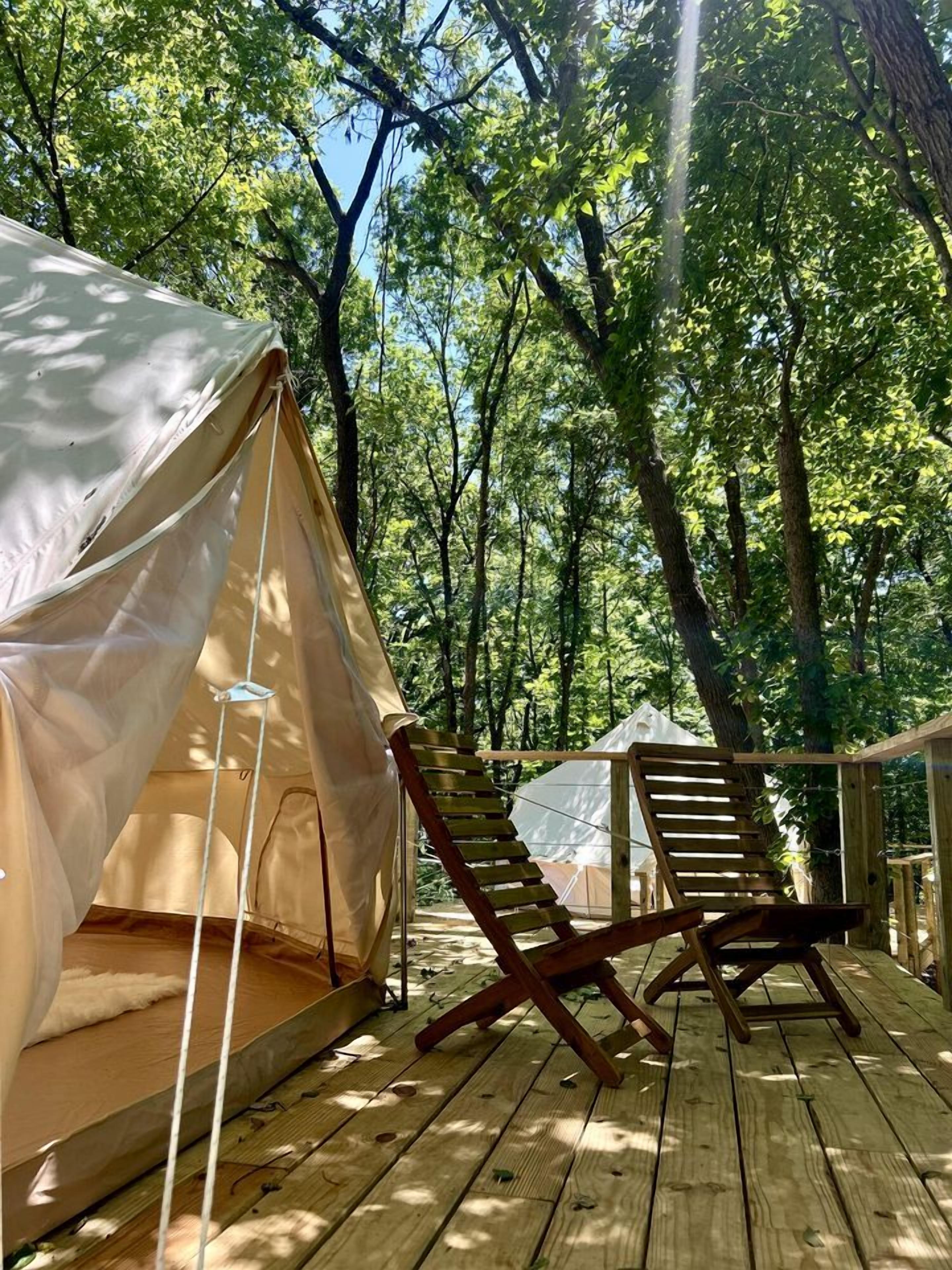 A tented accommodation with a wooden deck, a chair, and a view of the forest.