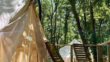 A tented accommodation with a wooden deck, a chair, and a view of the forest.