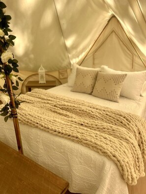 A tented room with a bed, pillows, a blanket, and a bedside table.
