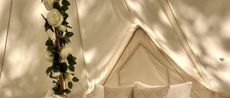 A tented accommodation with a bed, pillows, and a decorative plant.