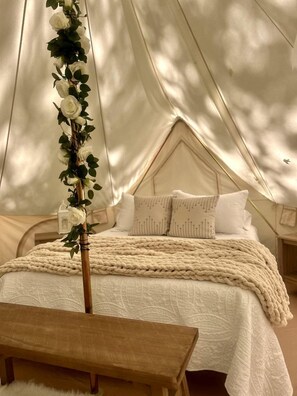 A tented accommodation with a bed, pillows, and a decorative plant.