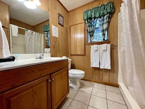 Un baño con paredes de madera, un inodoro blanco, un lavabo con espejo y una cortina de ducha.