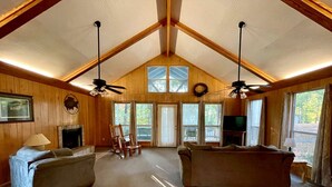A spacious living room with high ceilings, wooden walls, two couches, a fireplace, and a television.