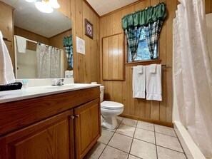 Een badkamer met houten wanden, een wit toilet, een wastafel met spiegel en een douchegordijn.