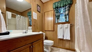 A bathroom with wooden walls, a white toilet, a sink with a mirror, and a shower curtain.