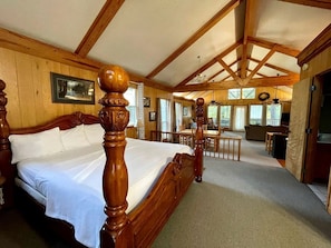 Dormitorio con estructura de madera, cama grande, zona de comedor y vistas al exterior.