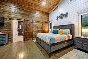 Ein Schlafzimmer mit Holzboden, einem großen Bett mit gemusterten Textilien, einem Schminktisch und einem an der Wand befestigten Fernseher.