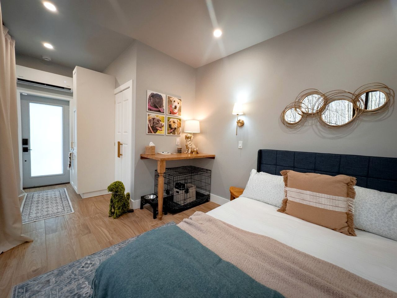 Une chambre à coucher avec un lit, un bureau doté d’une lampe, un petit chien et une porte donnant sur un balcon.