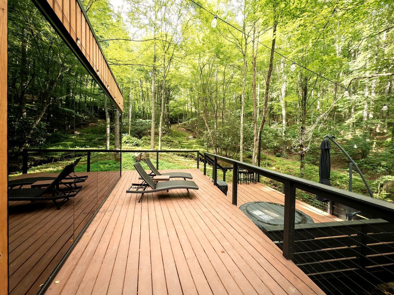 A wooden deck with lounge chairs and a table, surrounded by a forest.