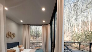 Quarto com cama, mesa de cabeceira e vista para o exterior.