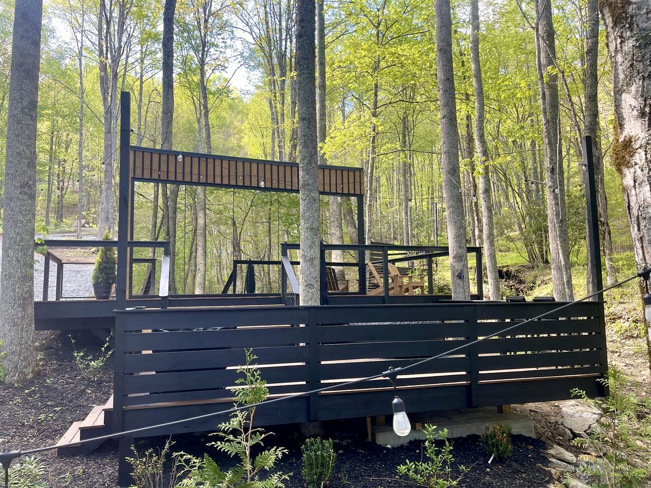 Une terrasse en bois, agrémentée de bancs et d’une table, entourée d’arbres.