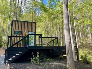 A wooden cabin with a staircase leading to a deck, surrounded by trees.