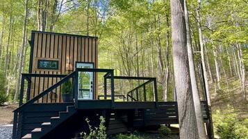A wooden cabin with a staircase leading to a deck, surrounded by trees.