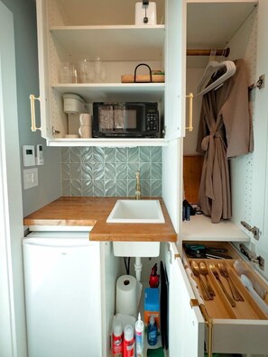 A compact kitchenette with a microwave, sink, and storage shelves.