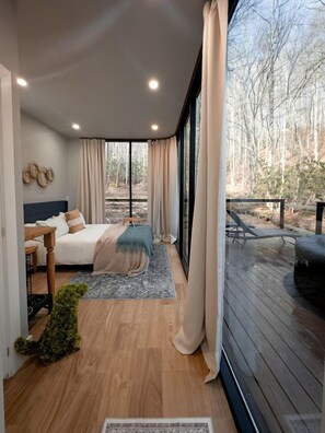 A bedroom with a bed, bedside table, and a view of the outdoors.