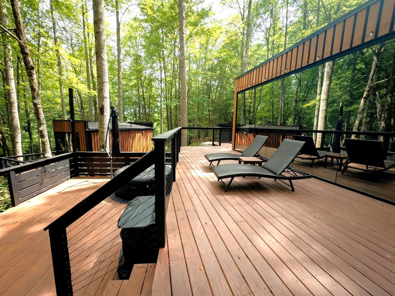 A wooden deck with lounge chairs, a bench, and a railing overlooking a forest.