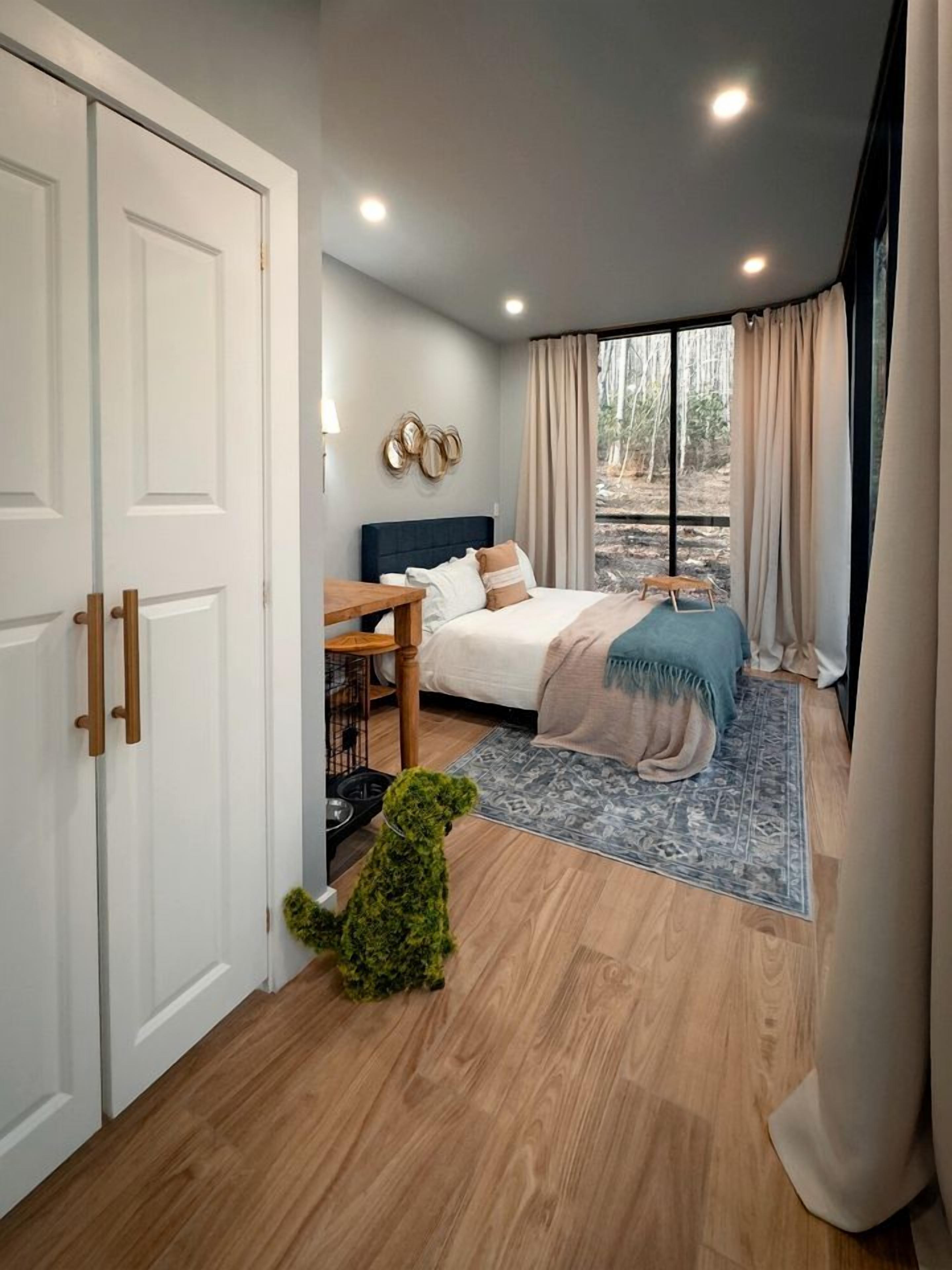 Een slaapkamer met een bed, een klein tafeltje, een kamerplant en uitzicht op het buiten.