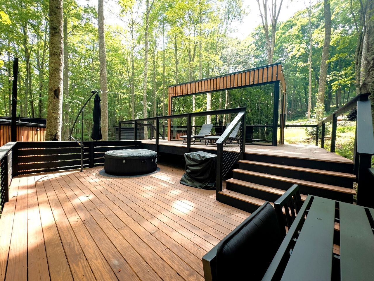 Une terrasse en bois avec des sièges extérieurs, un escalier et une vue sur la forêt.
