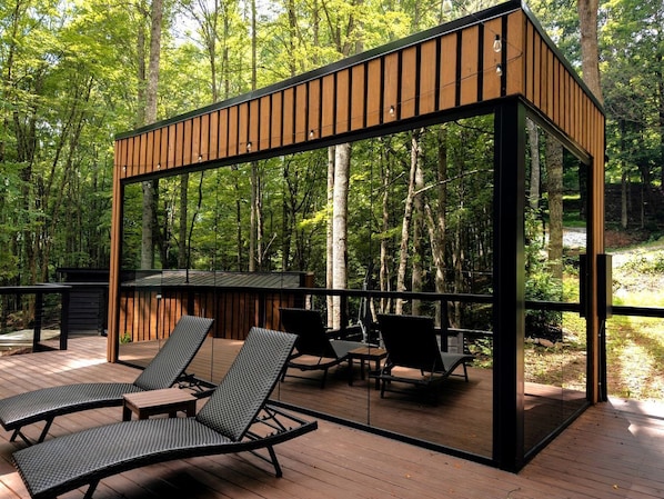 A modern outdoor deck with wooden railings, lounge chairs, and a glass enclosure.