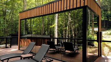Een modern terras buiten, met houten leuningen, lounge fauteuils en een glazen overkapping.