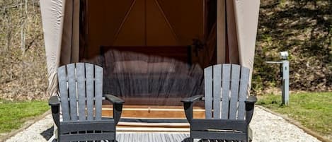 A tent with a platform and two chairs in a forest setting.