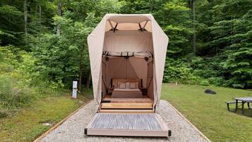 A tent with a bed inside, surrounded by a forest.