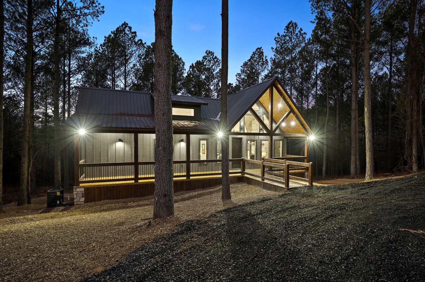 A cabin with a wooden deck, large windows, and a metal roof, surrounded by trees.