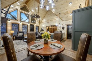 Ein Holzblockhaus-Innenraum mit Esstisch, gedeckt für vier Personen, einem Wohnbereich mit Sofa und Sesseln sowie einer Küchenzeile.