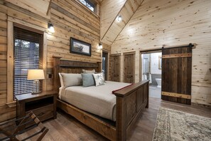Ein Holzblockhaus-Interieur mit einem Bett, einem Nachttisch, einer Lampe und einem gerahmten Bild an der Wand.