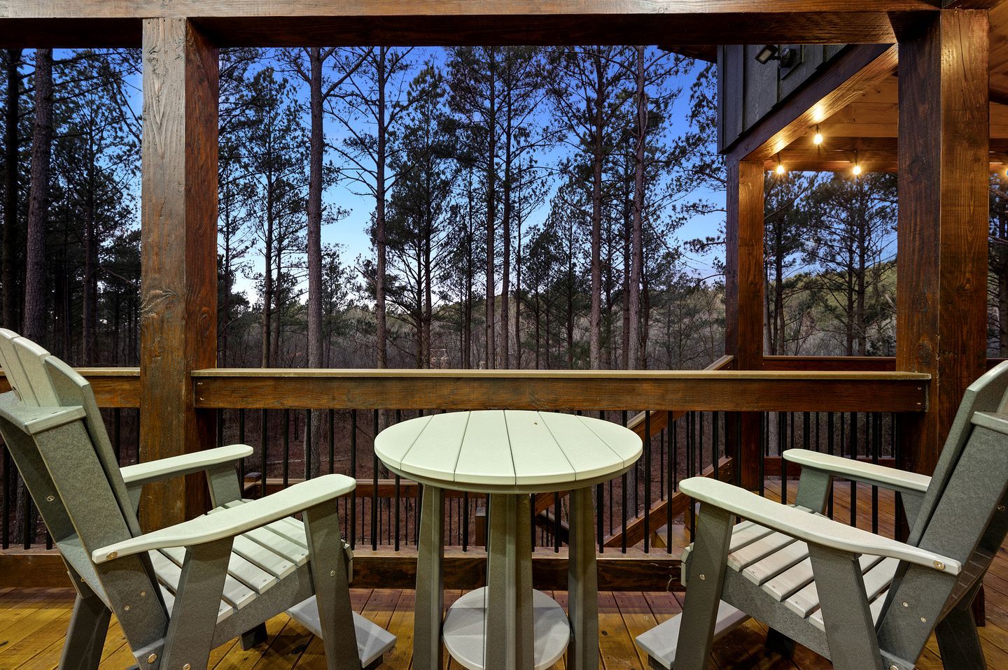 Terraza de madera con dos sillas y una mesa, con vista a un bosque.