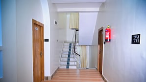 Un pasillo con una puerta de madera con la leyenda '205', un extintor y una escalera con alfombra a rayas.