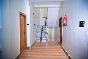 Un pasillo con una puerta de madera con la leyenda '205', un extintor y una escalera con alfombra a rayas.