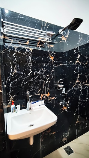 Un baño con pared de mármol negro, lavabo blanco, cabezal de ducha de mano y un dispensador de gel antibacterial.