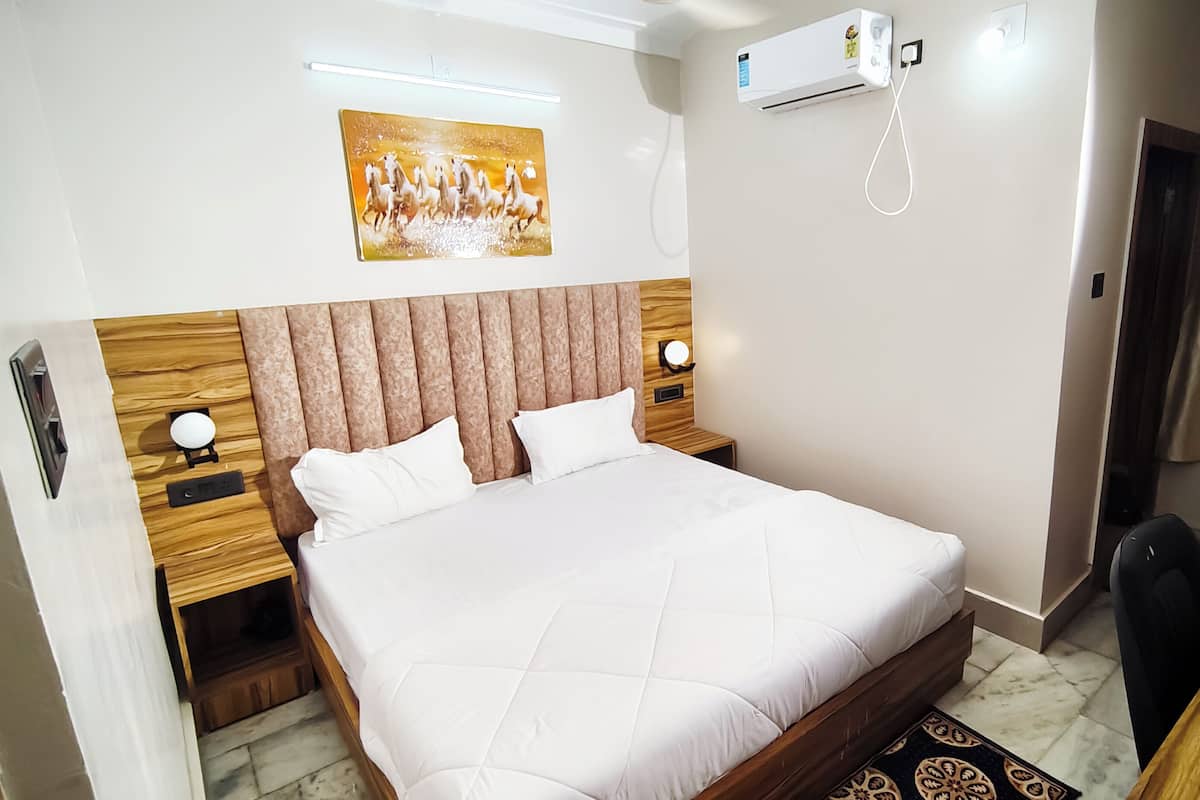 Hotellihuone, jossa on suuri sänky, puinen pääty, yöpöydät, seinälle asennettu ilmastointilaite ja taulu sängyn yläpuolella.