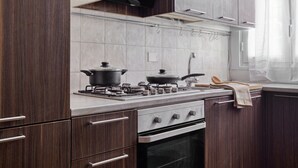 Uma cozinha moderna com armários de madeira, fogão a gás, exaustor e uma janela com cortinas leves.