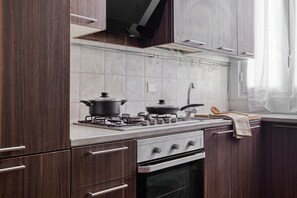 Eine moderne Küche mit Holzschränken, einem Gasherd, einer Dunstabzugshaube und einem Fenster mit durchsichtigen Vorhängen.