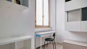 Quarto com escrivaninha branca, cadeira, radiador, janela e armário embutido.