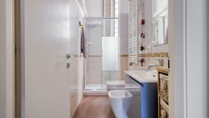 Casa de banho moderna com cabine de duche em vidro, sanita branca e lavatório com bancada azul.