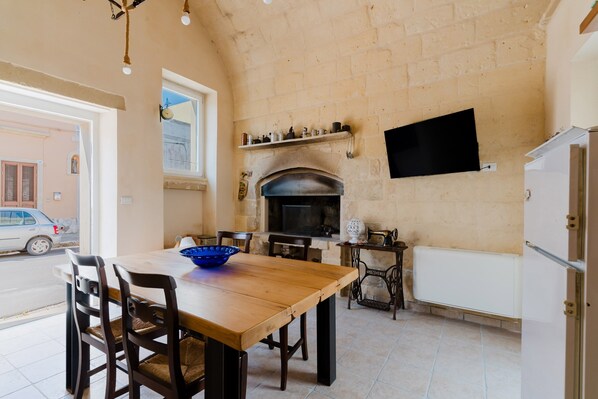 A dining area with a wooden table and chairs, a blue bowl, a fireplace, a television mounted on the wall, and a radiator.