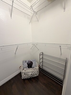 A laundry room with metal drying racks, a basket with a patterned bag, and a white wall. - Serene & Secure Condo | Gated Community, Pool, Gym, and Dedicated Parking (Henderson)