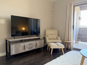 A modern living room with a flat-screen TV, a wooden entertainment unit, a cream-colored armchair, a small round table, and a fluffy white rug. - Serene & Secure Condo | Gated Community, Pool, Gym, and Dedicated Parking (Henderson)